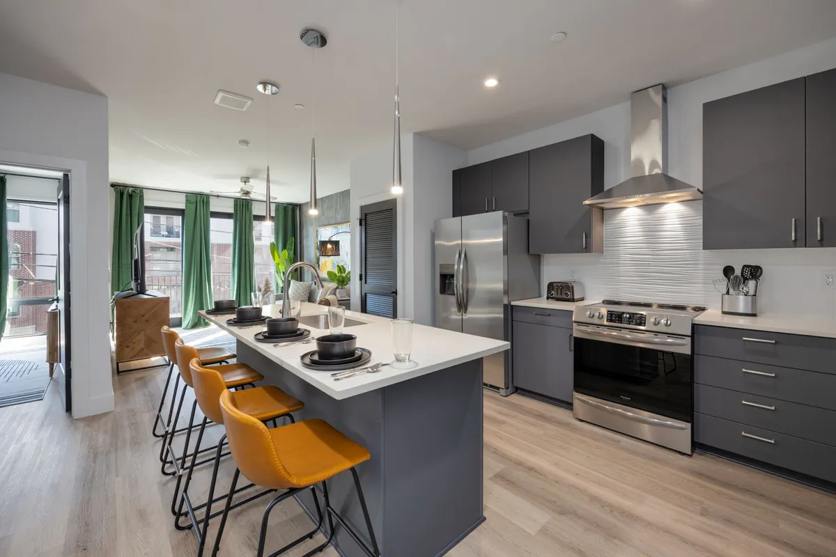 A modern kitchen featuring an island with bar seating, stainless steel appliances, and a window with green curtains. The island invites socializing, while the appliances and layout emphasize a functional and welcoming cooking space.