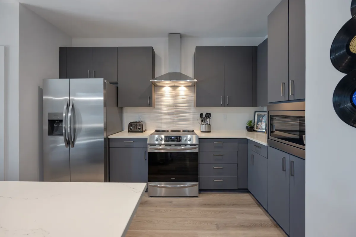 A bright, functional kitchen showcasing stainless steel appliances, stylish cabinetry, and a spacious countertop. The open layout suggests ease of movement and ample space for preparing meals or unpacking takeout.