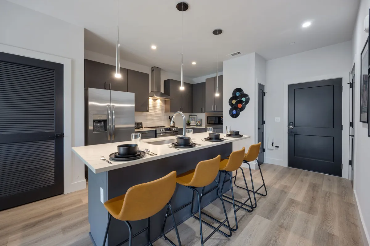 A contemporary kitchen highlighted by a central island with seating, stainless steel appliances, and decorative wall art. The space is set up for both cooking and casual entertaining, blending functionality with a welcoming atmosphere.