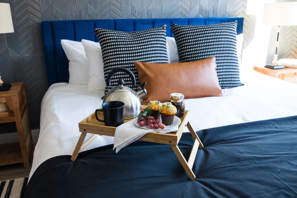 A plush bed with a blue upholstered headboard, plaid pillows, and a breakfast tray set atop the covers. The room exudes comfort and indulgence, perfect for relaxing or enjoying a quiet morning meal.