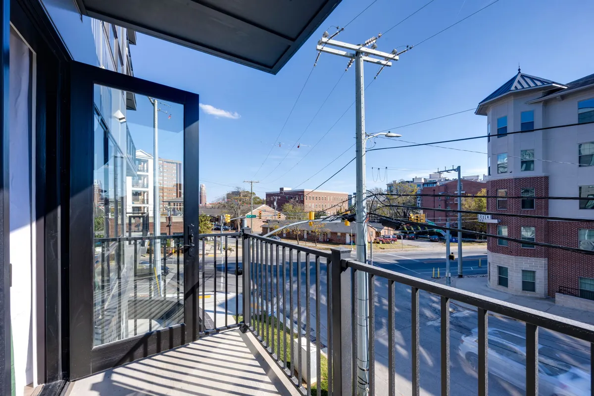This image shows a private balcony with a railing and expansive city views, accessible through an open door. The balcony is bathed in natural light, inviting residents to enjoy morning coffee or evening cocktails outdoors with a stunning Midtown backdrop.