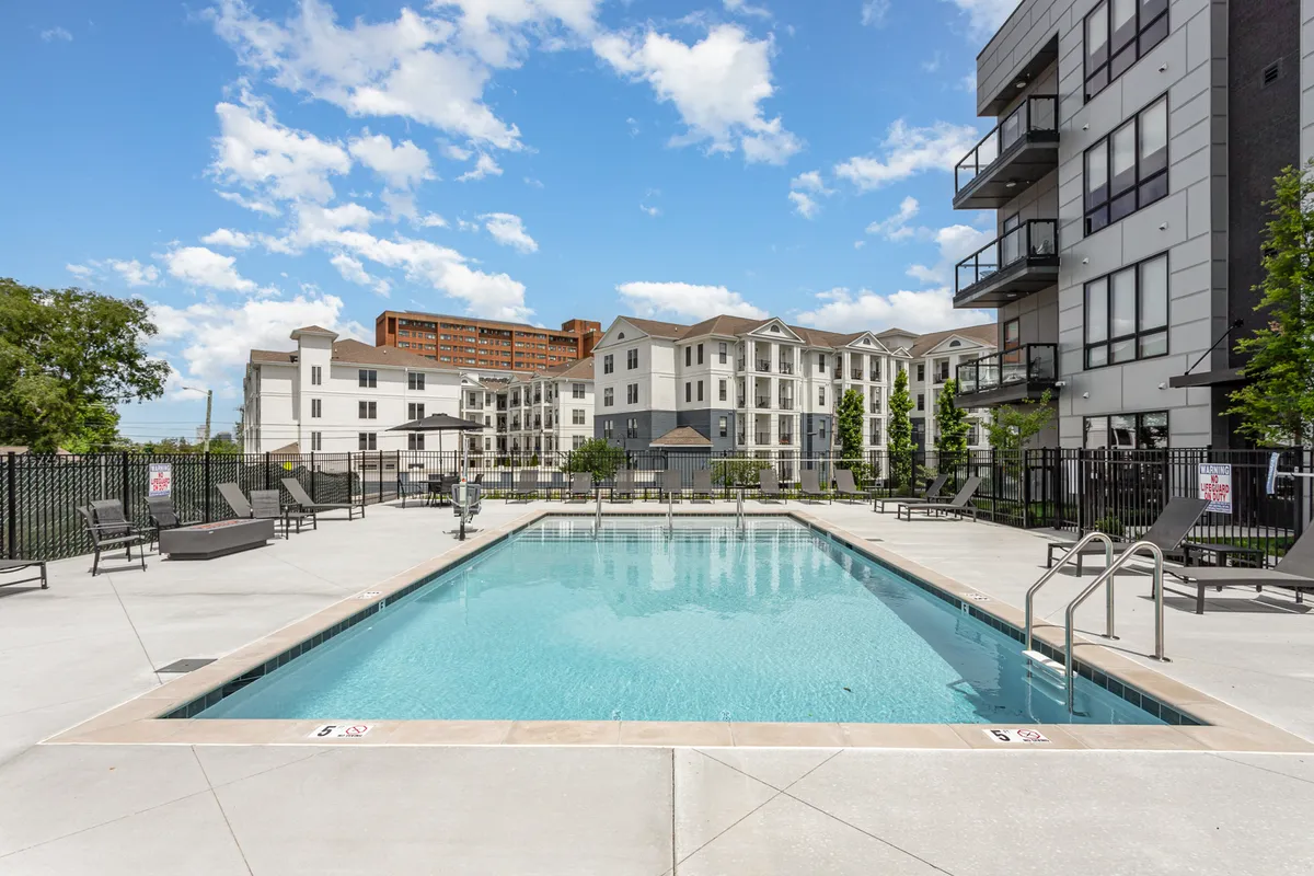 An inviting exterior pool area with lounge chairs, surrounded by the building's architecture and green landscaping. The scene emphasizes both relaxation and the option for community events.